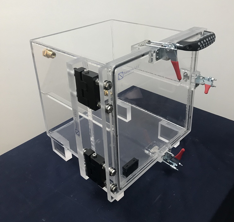 Clear acrylic desiccator cabinet with an airtight door, door clamps, digital hygrometer, and gas ports storing moisture-sensitive components